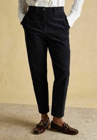 Tumši zili korduroveida bikses ar piegriezuma ērtumu, ar pogu aizdari, sānu kabatām un mīkstu tekstūru. Valkātas kopā ar spīdīgiem bordo loaferiem.