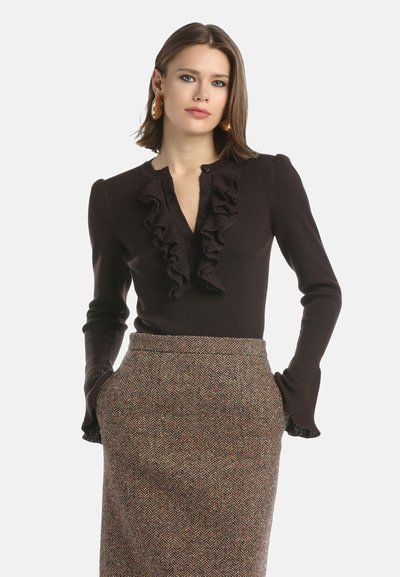 Hnedý rebrovaný sveter s volánikmi, dlhými rukávmi a zapínaním na gombíky, v kombinácii s textúrovanou sukňou so vzorom psie zuby a farebnými akcentmi.