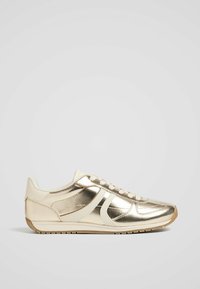 Metalen gouden sneakers met beige accenten, gladde textuur, afgeronde neus en rubberen zool met patroon en vetersluiting.
