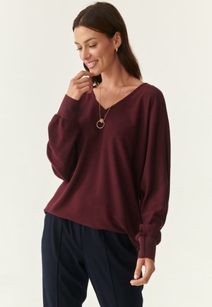 Burgundy V-pääntie paita, jossa on puffahtuet hihat, pehmeä kangas ja rento istuvuus. Yhdistetty tummiin housuihin sekä minimalistiseen kultaketjuun.