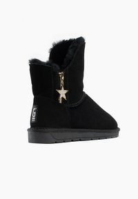 Botas de tobillo de ante negro con forro de pelo sintético, cremallera lateral y detalle de charm en forma de estrella dorada. Suela de goma gruesa para mayor tracción.