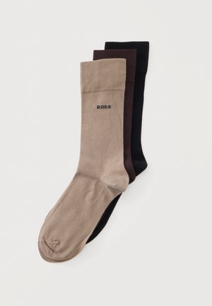 Trois paires de chaussettes unies en beige, brun foncé et noir, avec le mot "BOSS" sur le bord-côte de la chaussette beige.