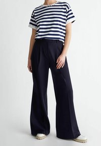 Camiseta de rayas en navy y blanco con mangas cortas y cuello redondo, combinada con pantalones negros de pierna ancha y cintura alta, y zapatillas blancas.