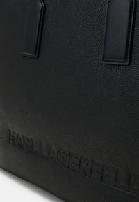 Sort pebret læder tote med prægede logo, to top hanke og mærkedetalje. Har en tekstureret overflade for holdbarhed og stil.