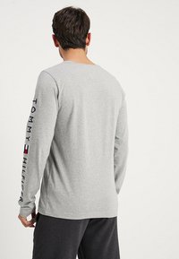 Graues Langarmshirt aus Baumwollmix mit dem "TOMMY HILFIGER"-Logo an der linken Ärmelseite, entspannt sitzend und mit Rundhalsausschnitt.
