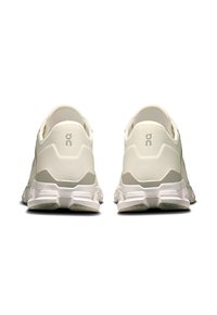 Baskets de sport blanches avec une tige en maillage texturé et un talon renforcé. Semelles douces avec des motifs de crans et logo de la marque à l'arrière.