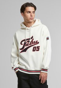Hvit hettegenser med hette, med stort svart og rødt grafisk tekst "Fubu 05" på forsiden, samt ribbestrikkede striper på mansjetter og midje.