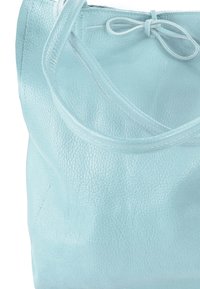 Lichtblauwe leren totebag met textuurafwerking, twee schouderbanden en een geplooide opening met een decoratieve knoopdetail.