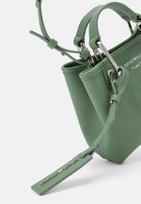 Zielona torebka skórzana o fakturowanej powierzchni, z dwoma uchwytami, srebrnymi akcesoriami i odpinanym tagiem z nazwą marki. Kompaktowy i zorganizowany design.