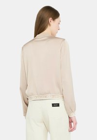 Blusa in satin beige con elastico a coste e logo "LIU-JO". Texture liscia, maniche lunghe e vestibilità aderente.
