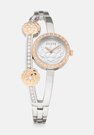 Round silver and rose gold watch with floral accents, crystal embellishments on the strap, and textured white dial. Adjustable bracelet design.