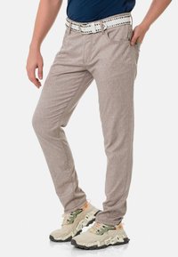 Hellbeige, strukturierte Slim-Fit-Hosen mit einem dezenten Muster, kombiniert mit einem weißen Gürtel mit metallischen Nieten und Sportschuhen.