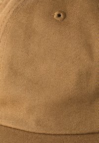 Bruine stoffen pet met een gestructureerd, geribd ontwerp en een centraal ventilatiegat. Het materiaal lijkt stevig en duurzaam.