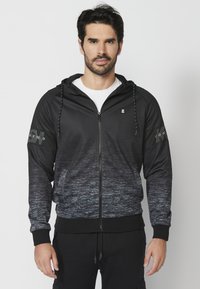 Čierna a šedá zipsová mikina s gradientovým dizajnom, textúrovaná tkanina, kapucňa so šnúrkou a potlačené akcenty na rukávoch.