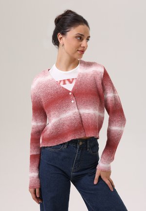 Rote und weiße kurz geschnittene Strickjacke mit gerippter Textur, Knopfverschluss und langen Ärmeln, kombiniert mit hochgeschnittenen dunklen Jeans.