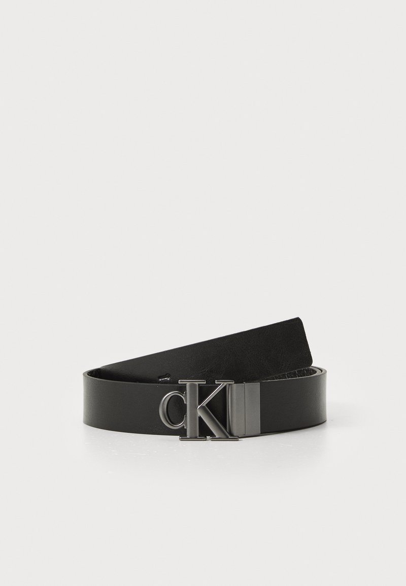 Zwarte leren riem met een gladde textuur en een metallic CK-logo gespsluiting. Het ontwerp heeft een klassieke, minimalistische vorm.