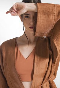 Bruine kimono-stijl jas met brede mouwen over een bijpassende bruine cropped top. De stof lijkt een textuur te hebben met een lichte, vloeiende kwaliteit.