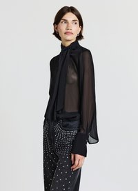 Schwarze, transparente Bluse mit Neckholder und langen Ärmeln, kombiniert mit dunklen Jeans, verziert mit silbernen Nieten. Weiche Textur, entspannte Silhouette.