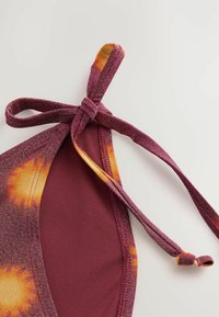 Maroon bikiniöverdel med knytning, som har ett klart orange och gult solstrålemönster längs kanten. Glänsande tygstruktur.