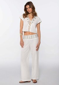 Top blanco cortado con escote en V y lazos, adornado con costuras decorativas. Pantalones blancos fluidos a juego con una cinturilla estampada.