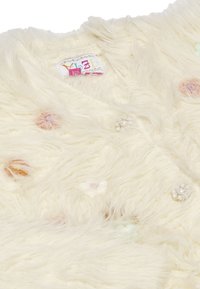 Tessuto bianco e fluffy con applicazioni floreali colorate e dettagli simili a perle. Etichetta visibile con informazioni sul marchio e sulla taglia.