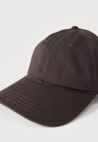 Casquette de baseball en coton marron foncé avec œillets de ventilation cousus et visière incurvée sur fond blanc.
