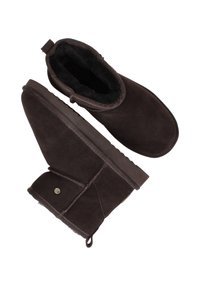 Bruine suède enkellaarsjes met shearling voering, ronde neus, versterkte hak en een zijknopdetail. Antislip rubberen zool.