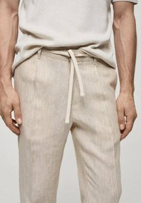 Lichtbeige, gestructureerde broek met verticale strepen, voorzien van een zachte drawstring tailleband en twee zijzakken. Casual ontwerp voor comfort.
