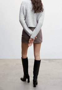 Suéter gris peludo, falda corta de cuadros y botas negras altas con tacón hasta la rodilla. El conjunto presenta un ajuste relajado y materiales texturizados.