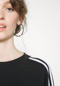 Felpa nera con collo rotondo, caratterizzata da strisce bianche sulle spalle. Il tessuto sembra morbido e leggermente strutturato.
