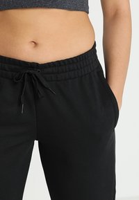 Zwarte trainingsbroek met een elastische tailleband en trekkoord, voorzien van zijzakken en een gladde, gestructureerde stof.