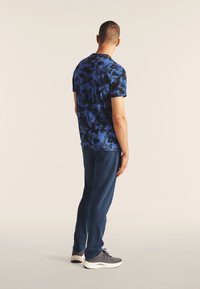 Camiseta de camuflaje azul de manga corta con cuello redondo, combinada con pantalones navy y zapatillas grises, con un diseño sencillo y un ajuste cómodo.