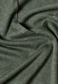 Tissu tricoté vert foncé doux et plié montrant une texture détaillée et des coutures fines.