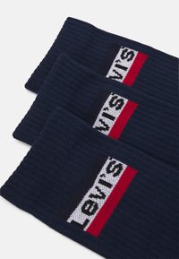 Jūras spēku zila ribota galvas lente ar taisnstūrveida logotipu ar baltām un sarkanām svītrām, uz kura skaidri redzams "Levi's" biezā fontā.