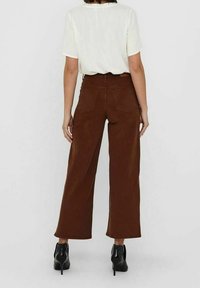 Bruine wijde broek met achterzakken, gemaakt van een zacht materiaal. Gecombineerd met een witte top met korte mouwen. Zwarte hoge hakken.