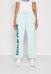 Světlemodré Nike tepláky s širokým střihem. Obsahují výrazné modré písmeno "NIKE AIR" na straně a stahovací pás na opasek.