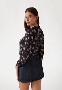 Blusa nera a fiori con fiori viola e bianchi, maniche lunghe, abbottonata ai polsini, abbinata a una minigonna in denim scuro.