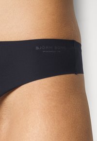Schwarze Bikini-Brief mit einem glatten, dehnbaren Stoff. Der Bund zeigt ein geprägtes Logo, hat einen niedrigen Schnitt und ein minimalistisches Design.