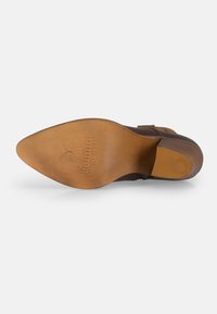 Suela de zapato de cuero marrón con acabado suave, texto del logo en relieve y forma curva. El tacón es de madera oscura con un borde plano.