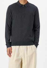 Mörkgrå långärmad polotröja med en delvis dragkedja, krage och ribbad kant. Bärs med ljusa byxor. Mjuk textur.