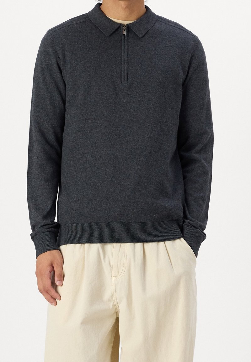 Mörkgrå långärmad polotröja med en delvis dragkedja, krage och ribbad kant. Bärs med ljusa byxor. Mjuk textur.