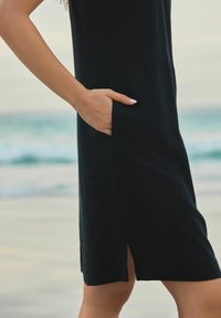 Robe en lin noir avec une poche latérale, coupe mi-genoux et une petite fente à l'ourlet pour faciliter les mouvements. Texture lisse.