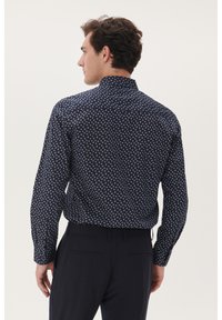 Marineblauw overhemd met kleine witte bloemenprint, lange mouwen en een klassieke kraag; gedragen met donkere broek, met een getailleerd ontwerp.