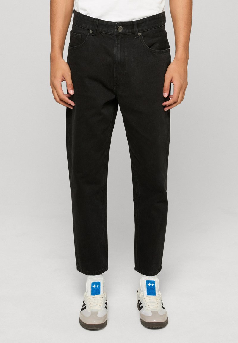 Fekete farmernadrág egyenes szárú szabással, elöl zsebekkel, övbújtatókkal és klasszikus felső gombbal. Kényelmes, laza szabás.