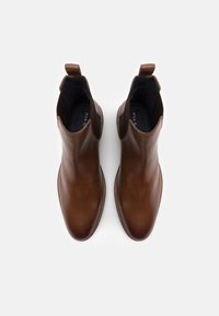 Hnědé kožené kotníkové boty s hladkým povrchem, elastickými bočními panely a poutky na stažení. Špičatá špička a kontrastní prošívání.