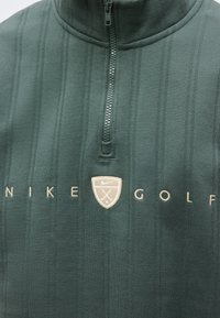 Σκούφος πράσινος γκολφ Nike με κάθετες ρίγες, φερμουάρ τριών τετάρτων και μπεζ κεντημένο λογότυπο και κείμενο στο στήθος.