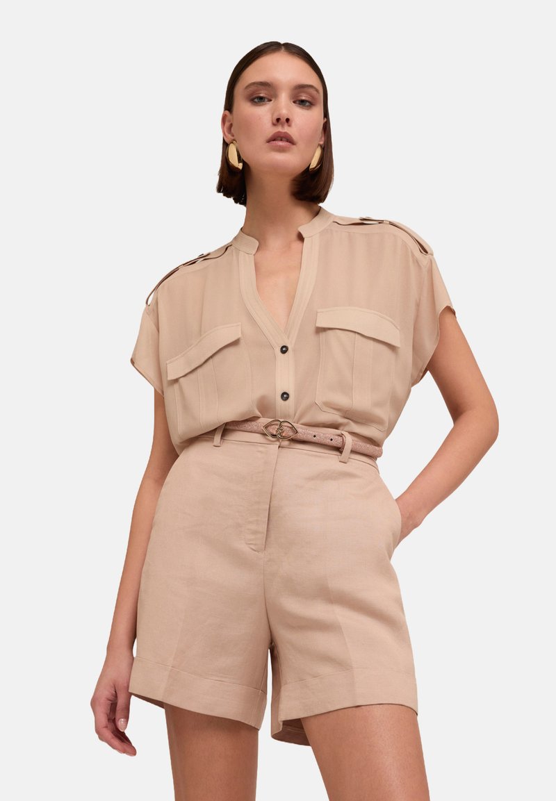 Beige kortärmad skjorta med framfickor och knäppning, kombinerad med högmidjade beige shorts och ett smalt bälte med en dekorativ spänne.