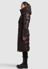 Pikk, tumesinine pruunine sulejope pehme, tekstuurse fliiskattusega, vööga taljeosas ja suure kapuutsiga. Omab tõmblukuga taskuid ja logomärki.