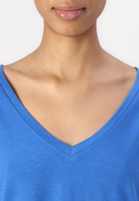 T-shirt blu a scollatura a V con una consistenza morbida e una leggera lucentezza, caratterizzata da una vestibilità regolare e bordi puliti attorno alla scollatura.