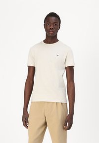 Lys beige bomull t-skjorte med rund hals, korte ermer og liten logo detalj på brystet, parret med lysebrune bukser.